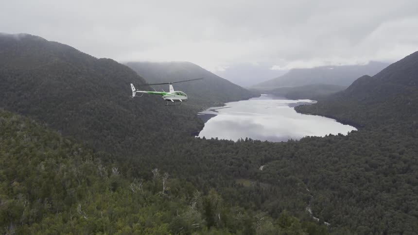 A helicopter flies over a lake in the mountains