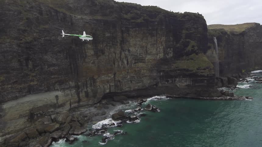 A helicopter flies over a rocky coast