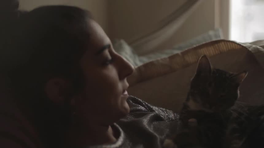 A woman with a cat laying on her while she speaks