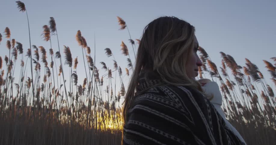 Woman walks in a large field as the sun sets