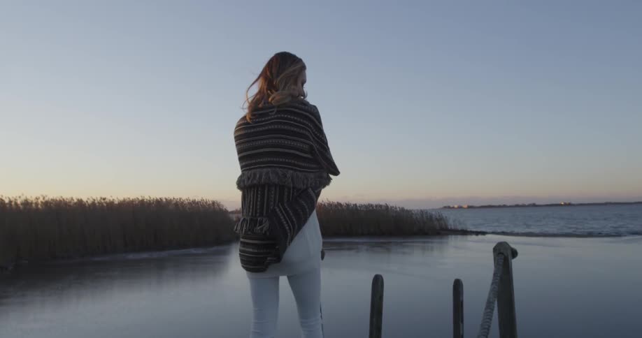 Woman walking on a dock in front of a lake at sunset