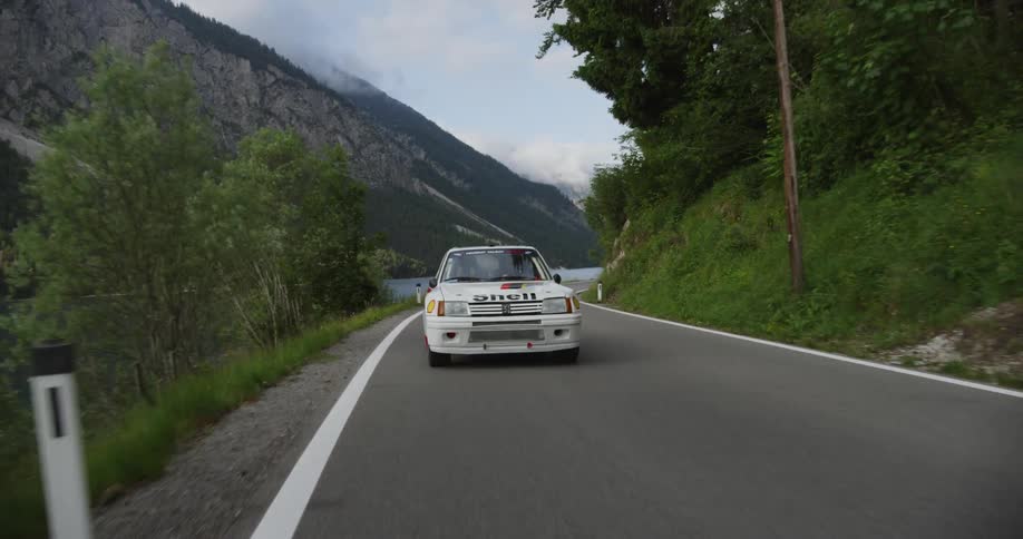 White car drives on a winding country road next to a body of water