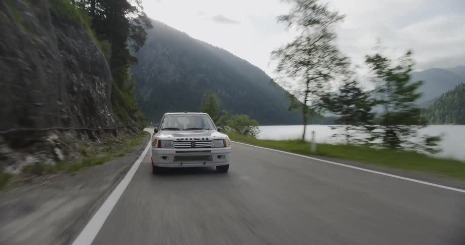 White car with decals travels down a highway near a lake