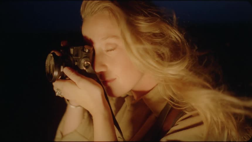 The wind blows a woman's hair as she takes a photograph at night