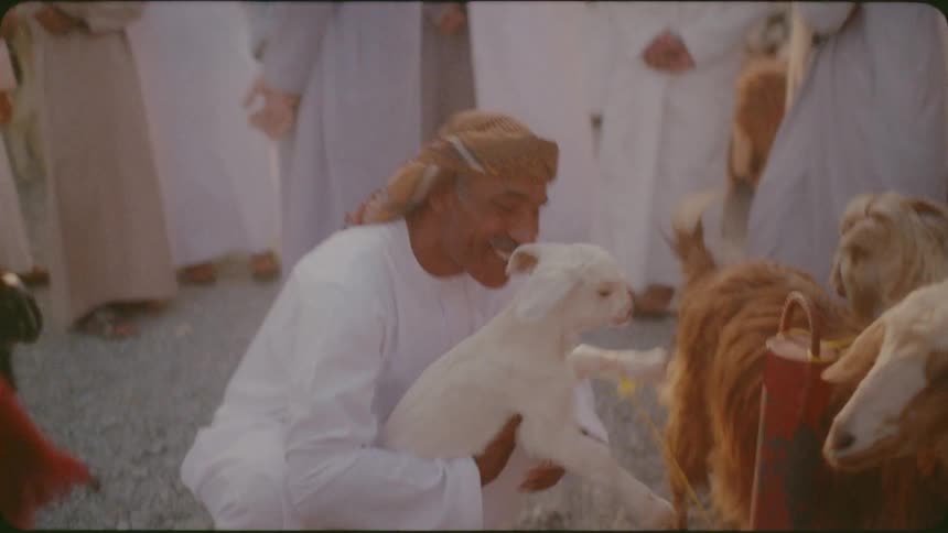 A man is picking up and nuzzling a lamb in a market in daylight