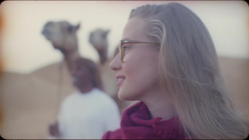 Woman wearing glasses walks with a man that is leading camels