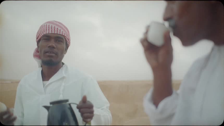 Men drink out of small tea cups in the desert