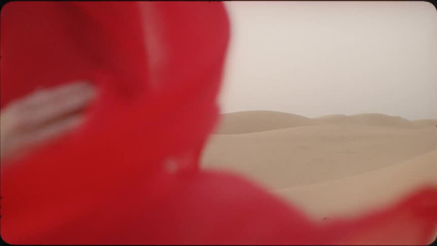 A woman wears a red sheet over her face in the desert