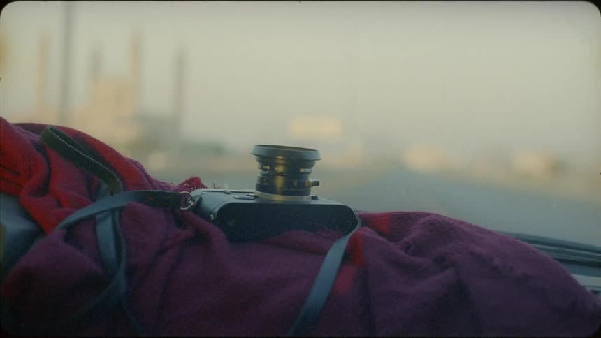 Camera with a strap attached sits on a red blanket on the dashboard
