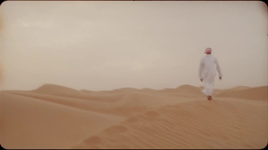 A man walks atop a sand dune in the desert