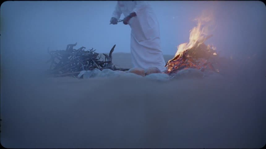 A man adds branches to a fire in the desert