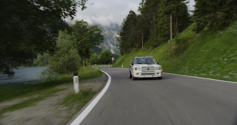 White vehicle drives on a curving country road near the mountains