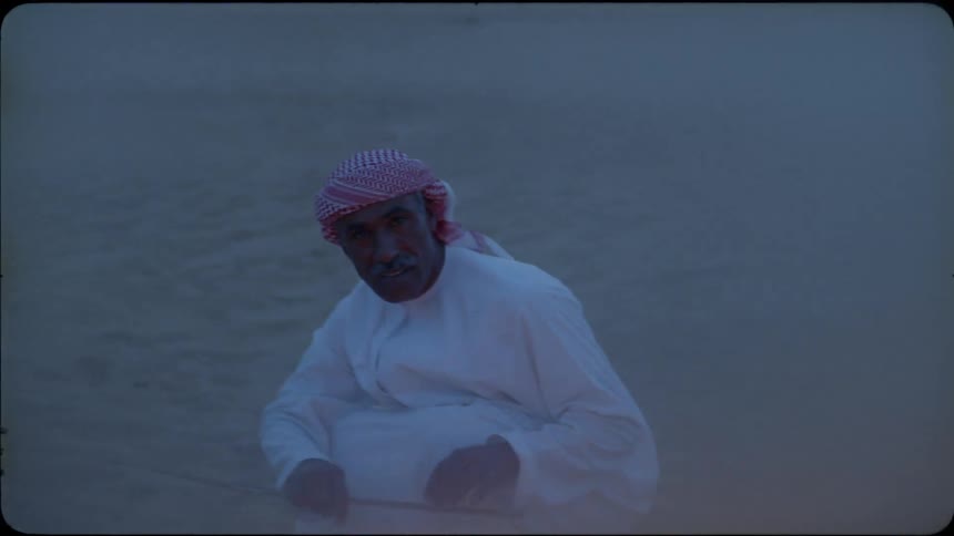 An Arab man stands up after feeding twigs to the campfire