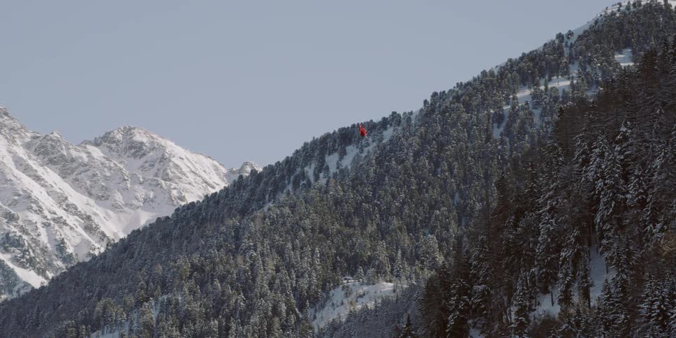 A red helicopter flies above the snowy mountains
