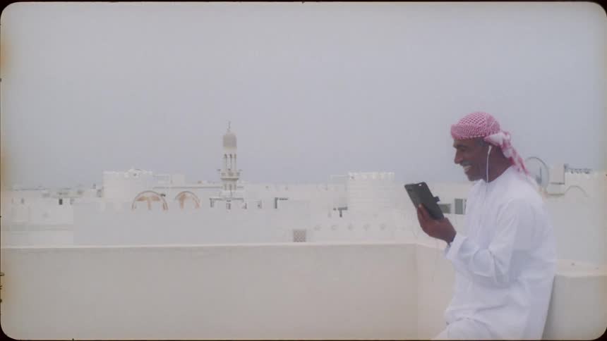 Man wearing a turban laughs as he looks at his cellphone under a cloudy sky