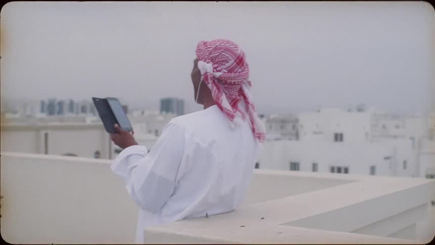 An arab man is standing on a rooftop talking on his cellphone in daylight