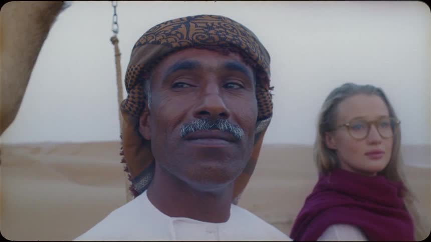 A man and woman stand by a camel in the desert