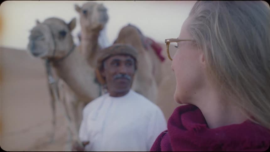 Man and woman talk near camels in a desert