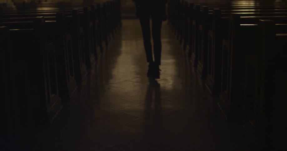 A woman walks the the aisle in a dark and empty church