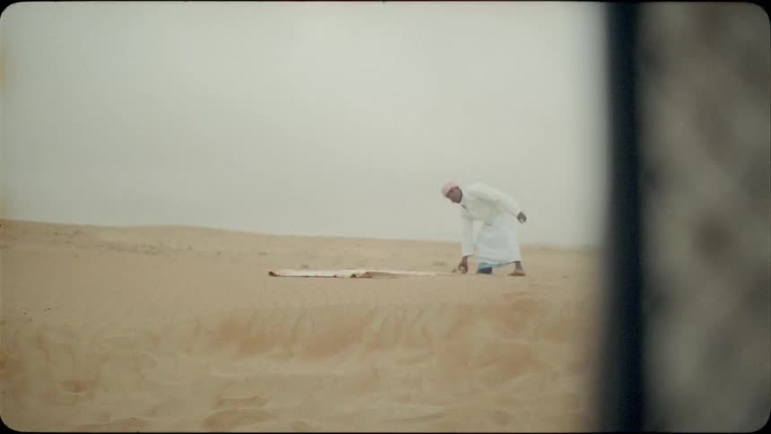 A middle eastern man lays a blanket in the sand