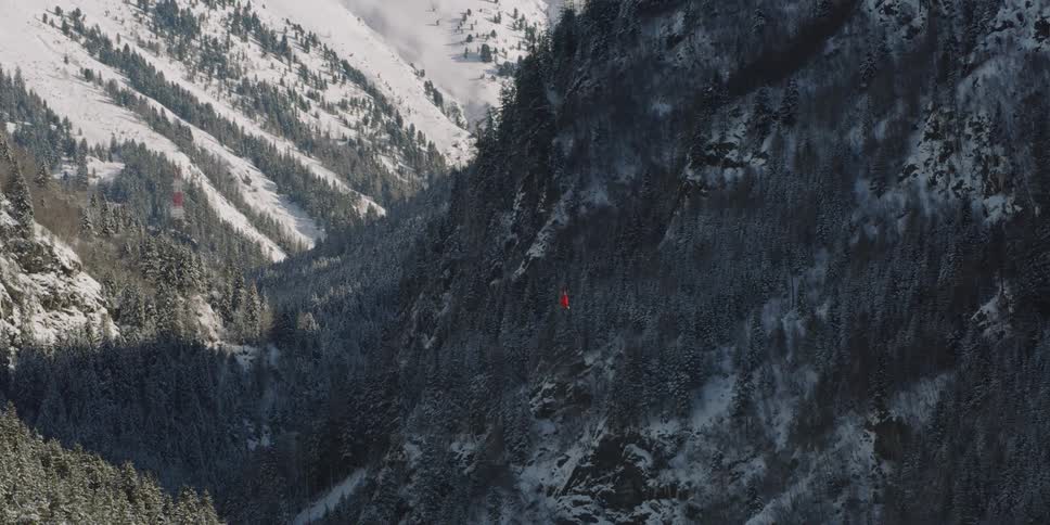 A helicopter flies over trees and mountain slope