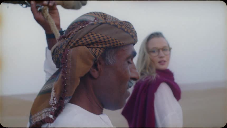 A blond haired woman walks with a middle eastern man in the desert