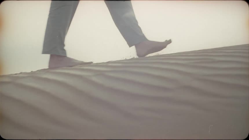 Woman walks in the desert and kicks up the sand with her feet