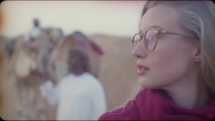 A blond haired woman walks with a middle eastern man in the desert
