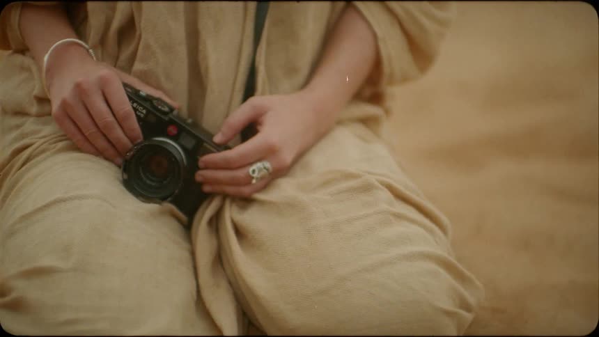 A woman is kneeling in the desert holding a camera in daylight