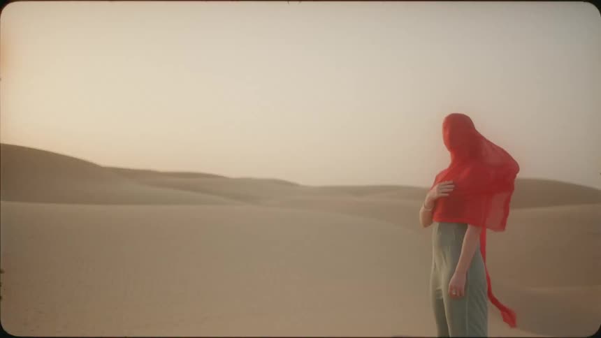 A woman has a red sheet over her face in the desert
