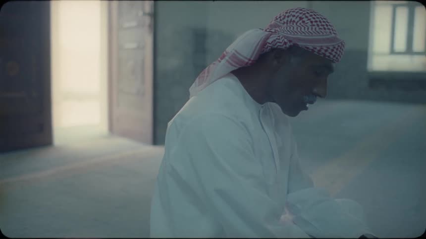 A man is sitting on the ground in a mosque during the day saying prayers