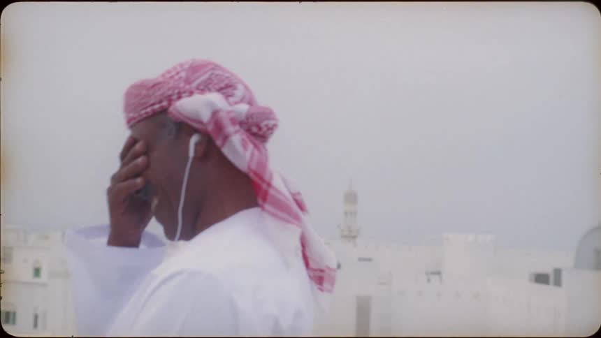 Man standing on a rooftop in a city smiles and covers his face with his hand