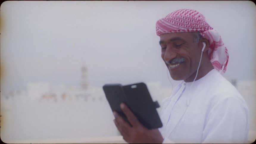 Man wearing ear buds laughs as he looks at his cell phone