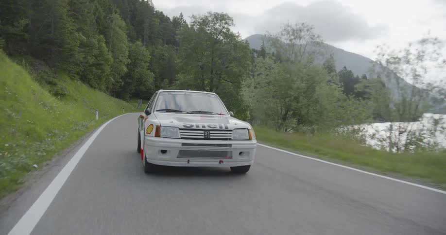 White vehicle drives on a winding country road next to a body of water