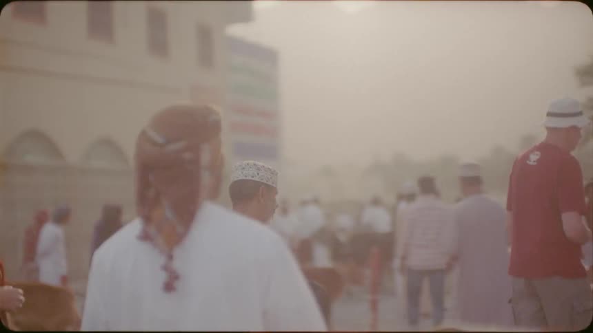 An arab man and a woman are walking through a livestock market outside in daylight