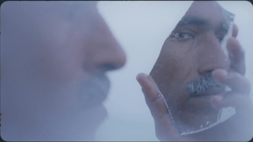 Man with a mustache looks at his reflection in a small mirror