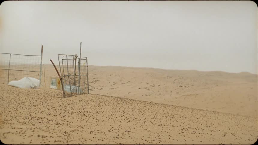 Rickety broken pieces of fence stand up on flat sandy land