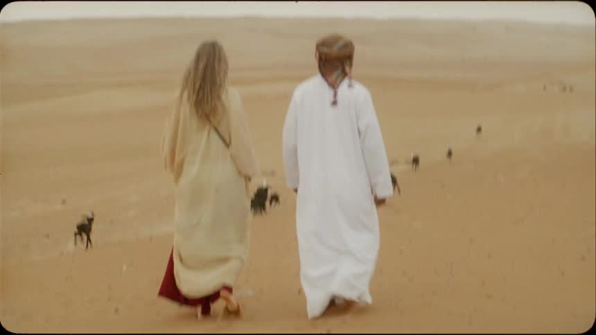 Man and woman walk in the desert as animals run next to them