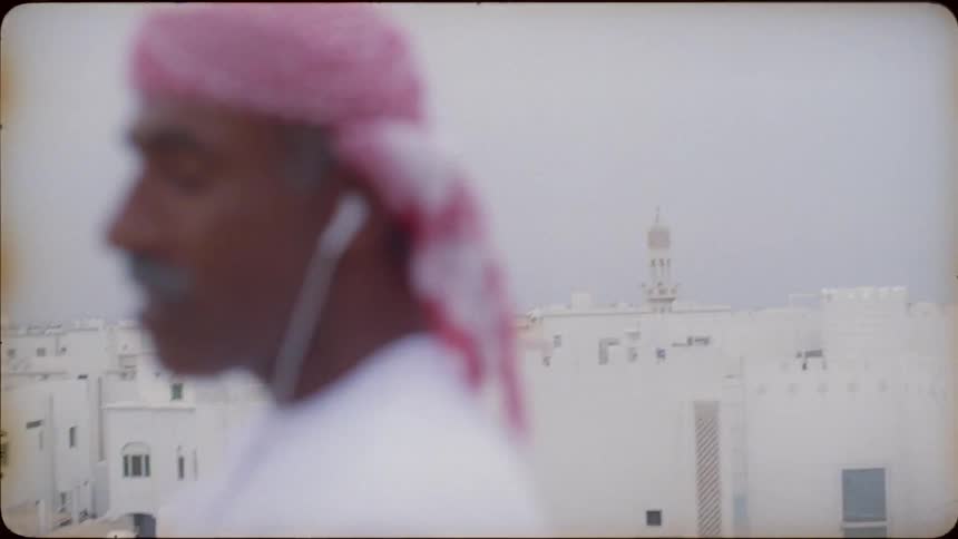 An arab man is standing on a rooftop talking on his cellphone in daylight