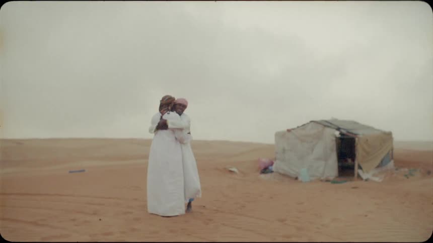 Two men greet each other and hug in the desert