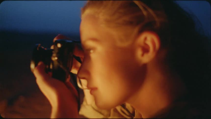 A blond haired woman takes a photograph at night