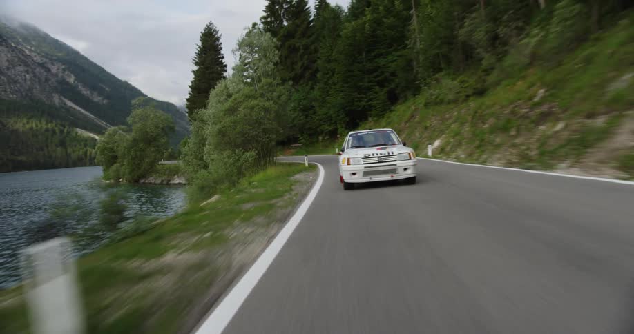 A race car travels on a rural road passing river, trees and hills