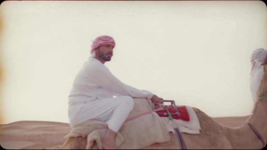 Men travel through the desert on camels