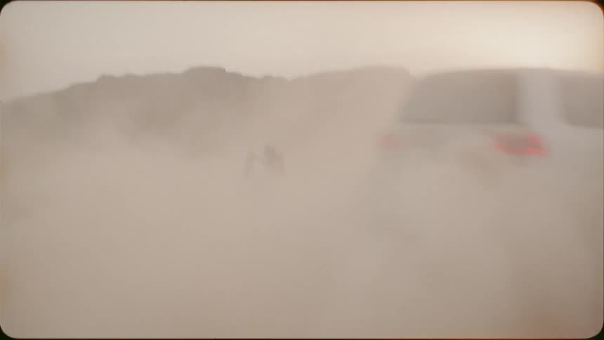 A man films a truck drifting in the sand