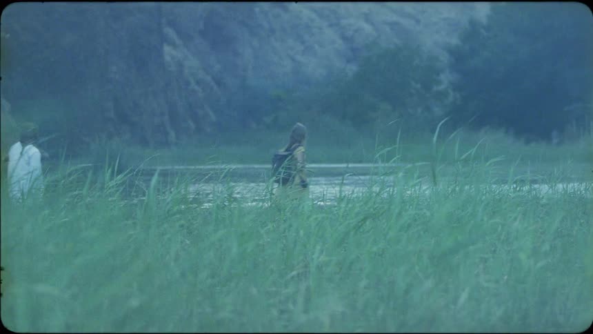 A woman is wading through the waters of a river with an arab man in daylight
