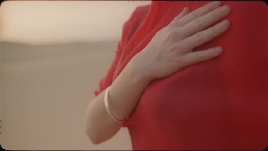 Woman wearing a gold bracelet stands with her hand over her heart