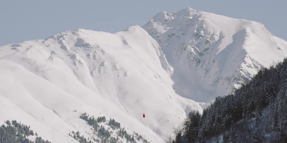 A red helicopter flies between two mountains