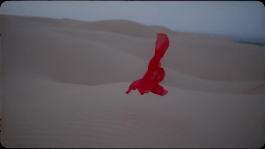 Red veil blows in the wind and lands on the sand in a desert