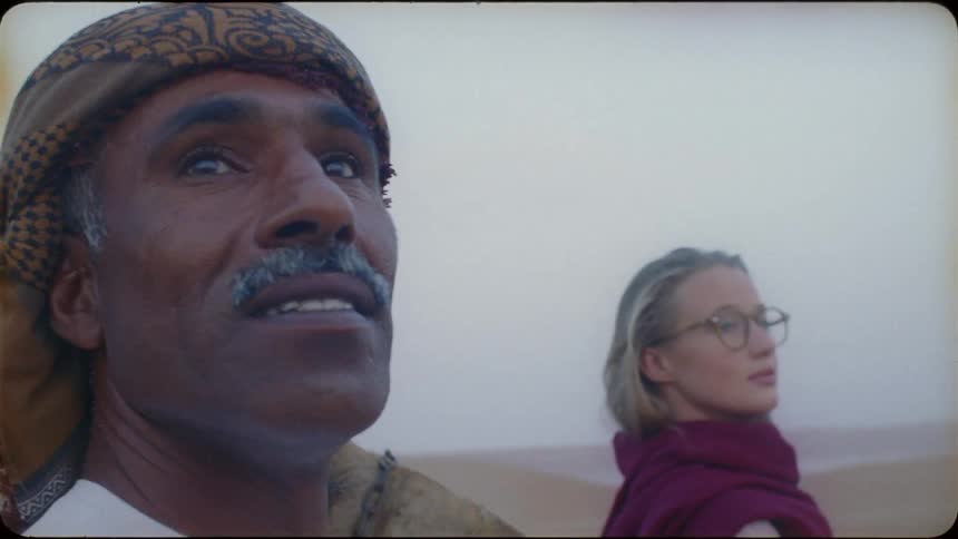 Man and woman stand in the desert with a camel