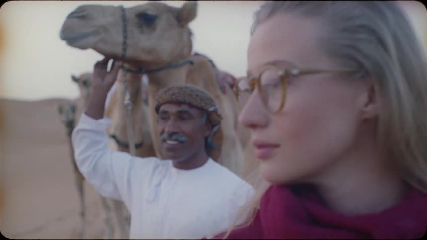 A blond haired woman stands in the desert with a man and camels